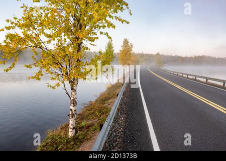 Finnische Landschaft mit schmaler Autostraße durch den See. Stockfoto