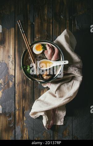 Traditionelle japanische Nudelsuppe mit Shiitake Pilze, Eier, Geschnetzeltes Rindfleisch und Grüns in Keramik Schüssel mit hölzernen Eßstäbchen und weiß Löffel serviert. Stockfoto