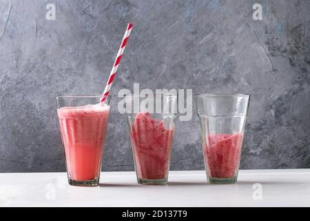 Rote früchte Beeren Wassermelone eisgekühlten Cocktail und gefrorenen Saft Sorbet in Gläsern mit gestreiften Stroh stehen auf weißem Marmor tisch mit grauen Wand an backgro Stockfoto