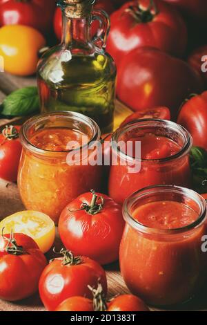 Vielfalt von drei hausgemachten Tomatensaucen in Gläsern mit Zutaten oben. Verschiedene Arten von Tomaten, Basilikum, Olivenöl, Pfeffer, Salz. Nahaufnahme Stockfoto