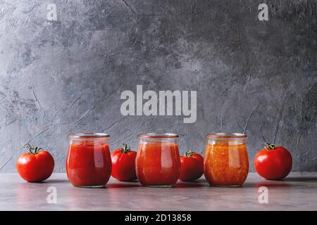 Vielzahl von drei hausgemachten Tomatensaucen in Gläsern mit Zutaten Tomaten oben über grau Küchentisch. Platz kopieren Stockfoto