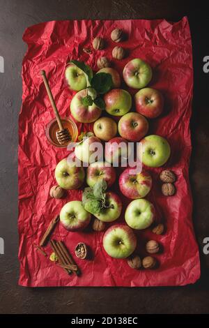 Reif Organic Gardening grün rote Äpfel mit Blätter, Nüsse, Zimt und Glas Honig auf Rot hell zerknittertes Papier über dunkle Textur Hintergrund. Flat l Stockfoto