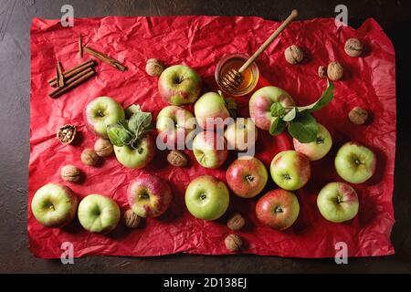 Reif Organic Gardening grün rote Äpfel mit Blätter, Nüsse, Zimt und Glas Honig auf Rot hell zerknittertes Papier über dunkle Textur Hintergrund. Flat l Stockfoto