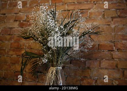 Vase mit kleinen weißen Wildblumen auf Ziegelwand Hintergrund, Café, Restaurant im Loft-Stil mit floralen natürlichen Dekoration Stockfoto