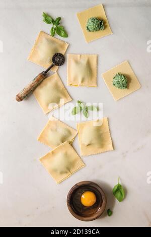 Hausgemachte Roh ungekocht italienische pasta Ravioli mit Spinat, Ricotta, Eigelb, Basilikum besetzt, Pasta Cutter. Weißer Marmor Hintergrund. Flach, Raum Stockfoto