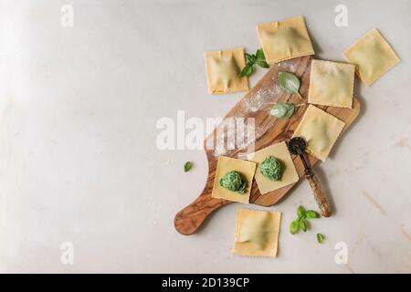 Hausgemachte Roh ungekocht italienische pasta Ravioli mit Spinat, Ricotta, Eigelb besetzt, Basilikum in Olivenöl Holz Schneidebrett. Weißer Marmor Hintergrund. Flach Stockfoto