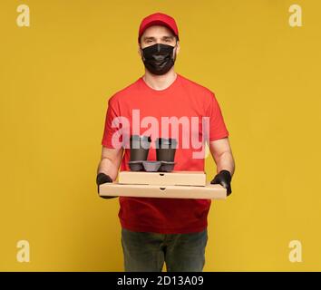Liefermann in roter Mütze, T-Shirt Uniform, Schutzmaske und Handschuhe isoliert auf gelb Stockfoto