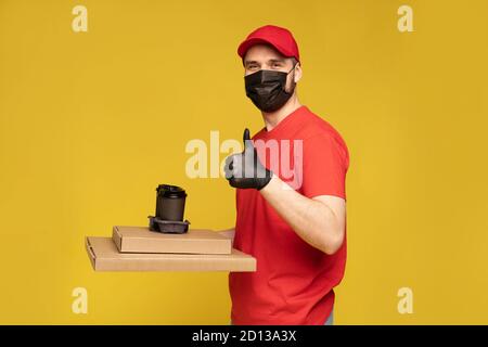 Liefermann in roter Mütze, T-Shirt Uniform, Schutzmaske und Handschuhe isoliert auf gelb Stockfoto