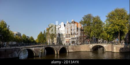 AMSTERDAM, NIEDERLANDE - Sep 22, 2020: Breite Kanalansicht der typischen Brücken und historischen Herrenhäuser in Amsterdam gegen einen klaren blauen Himmel mit whit Stockfoto