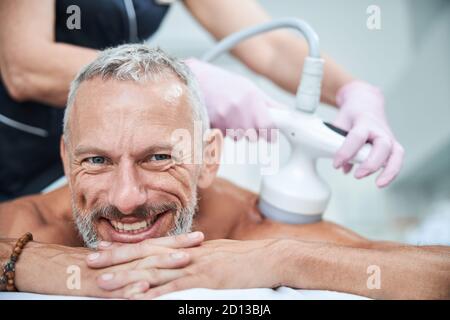 Smiley Senior Citizen auf dem Bauch während kosmetischer Eingriffe Stockfoto