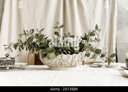 Dekorierter Boho-Tisch. Der Tisch ist mit einer Tischdecke bedeckt, auf der sich elegante Teller und Gläser befinden, eine Vase mit einer grünen Pflanze Stockfoto