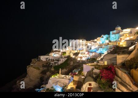 Die Nacht fällt auf das griechische Dorf Oia auf der Insel Santorini. Typische orthodoxe Kirche mit runden und blauen Dach überhängt die Stadt Stockfoto