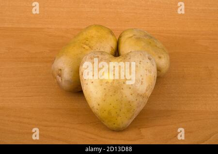 Kartoffeln auf einem Holztisch. Einer von ihnen ist in Form eines Herzens. Stockfoto