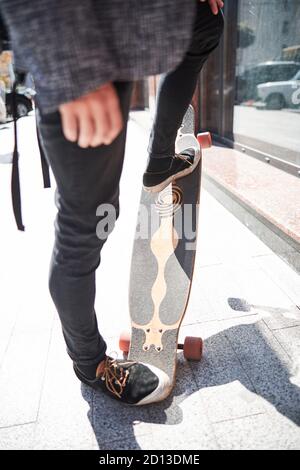 Gut gekleideter Mann, der mit seinen Füßen ein Longboard hochhebt Stockfoto