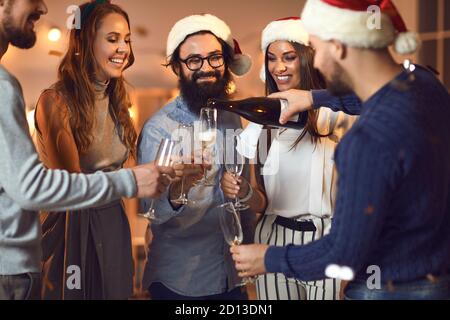 Junger Mann, der zu Weihnachten Champagner in die Gläser seiner Freunde gießt Oder Neujahrsparty Stockfoto