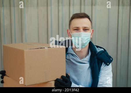 Happy Delivery Mann in einer Schutzmaske schaut auf die Kamera und hält zwei Boxen Stockfoto