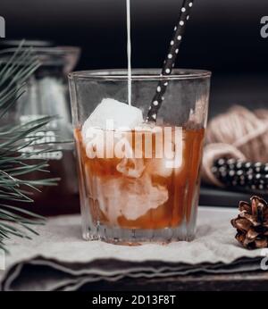 Bei der Zubereitung von kaltem Latte-Kaffee wird ein Rinnsal Milch in einen schwarzen Kaffee in einem durchsichtigen Glaskrug auf dunklem Hintergrund gegossen. Stockfoto