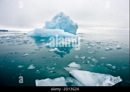 Eine weite, niedrige Ansicht von schmelzenden Meereisschollen In den stillen Gewässern der Nordarktischen mit dem Eisberg und der Eiszeit Wand im Hintergrund Stockfoto