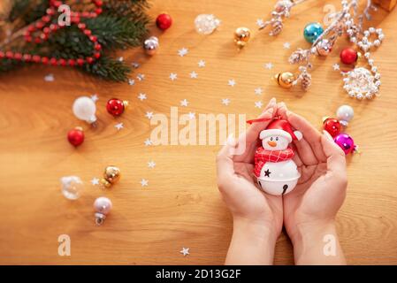 Weihnachtskonzept. Menschliche Hände halten eine weihnachtsdekoration in Form von Schneemann mit festlichen Lichtern und Weihnachtsschmuck auf dem Hintergrund Stockfoto