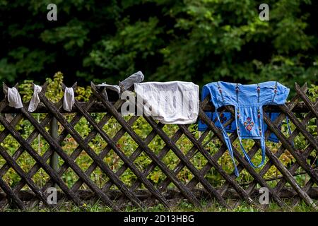 Hübsche bestickte Küchenschürze, Kissen und Socken hingen zum Trocknen an einem Zaun Stockfoto