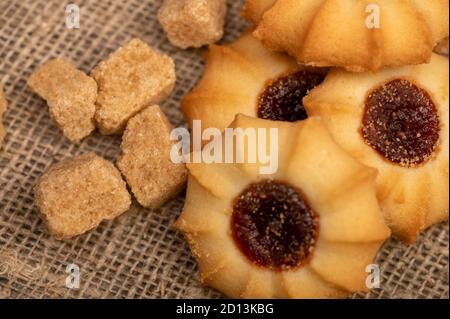 Hausgemachte Gebäck Cookies mit Marmelade und Stücke von braunem Rohrzucker auf einem Hintergrund von homespun Stoff mit einer rauen Textur, Nahaufnahme, selektive Fokus Stockfoto