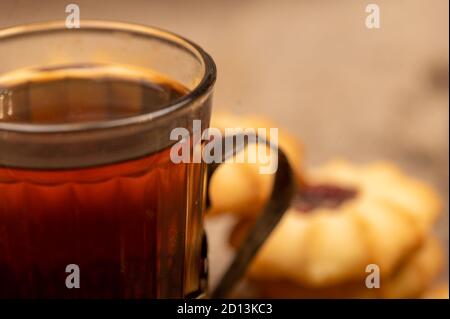 Hausgemachte Gebäck-Kekse mit Marmelade und einem facettierten Glas Tee in einem Vintage-Cup-Halter auf einem Hintergrund von homespun Stoff mit einer rauen Textur, close-up, Stockfoto