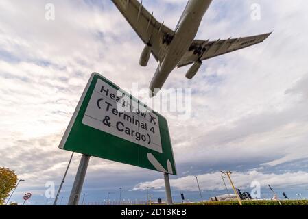 Schild für Heathrow Airport, London, UK, Terminal 4 und Fracht, mit einem Düsenflugzeug Landung, über A30 Straße. Abends Ankunft über Ortsschild Stockfoto