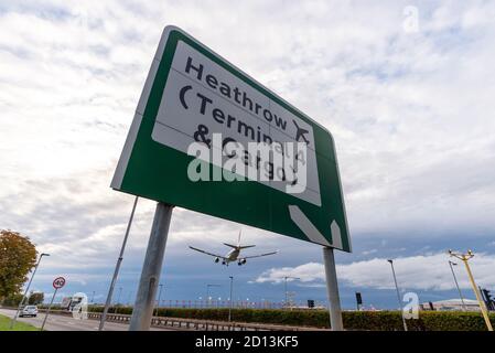 Schild für Heathrow Airport, London, UK, Terminal 4 und Fracht, mit einem Düsenflugzeug Landung, über A30 Straße. Abends Ankunft mit Straßenverkehr Stockfoto