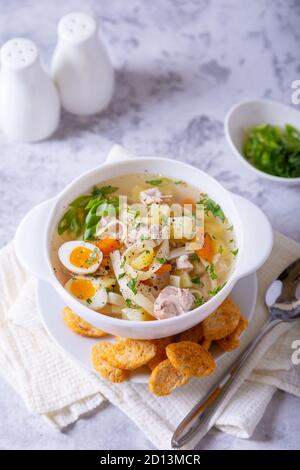 Suppe mit Hühnchen, Nudeln, Kartoffeln, Wachteleiern und Karotten. Gewürzt mit Zwiebeln und Petersilie. Nahaufnahme. Stockfoto