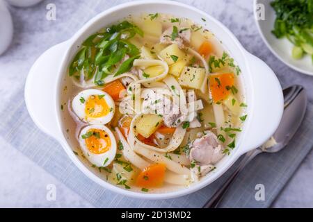 Suppe mit Hühnchen, Nudeln, Kartoffeln, Wachteleiern und Karotten. Gewürzt mit Zwiebeln und Petersilie. Nahaufnahme. Stockfoto