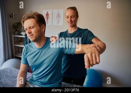 Junger Mann, der an Handverletzungen leidet, Stretching-Übung mit Physiotherapeutin Stockfoto