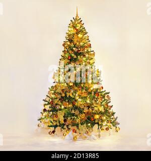 Weihnachtsbaum mit goldenen Ornamenten und schönen Lichtern. Studioaufnahmen. Reich dekorierter goldener Weihnachtsbaum auf pastellfarbenem Hintergrund. Reich Stockfoto