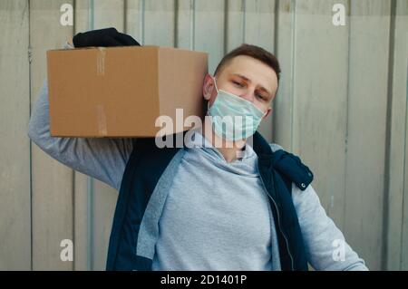 Der Lieferer in einer Schutzmaske hält die Box an Seine Schulter Stockfoto