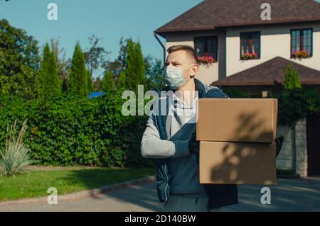 Lieferung Mann in Schutzmaske stehen mit zwei Boxen und Schaut sich um Stockfoto