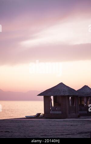 Bungalow an einem Sandstrand gegen einen rosa Sonnenuntergang in der Türkei. Exklusiver Urlaub am Meer. Stockfoto