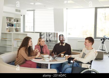 Seitenansicht auf multi-ethnische Gruppe von Studenten studieren in der College-Bibliothek mit jungen Mann mit Rollstuhl im Vordergrund, kopieren Raum Stockfoto