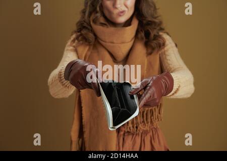Hallo september. Nahaufnahme einer unglücklichen Frau mittleren Alters im Schal mit Geldbörse und Lederhandschuhen vor bronzefarbenem Hintergrund. Stockfoto