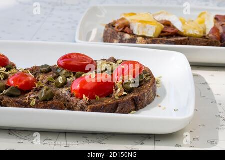 Köstliche italienische Bruschetta mit geröstetem Brot und mit Kirschtomaten, Basilikum und Knoblauch und geröstetem Brot mit frischem Käse, Honig und Speck Stockfoto