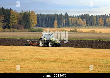 Bauer pflügt Feld mit grünen Valtra Traktor und Pflügen an einem sonnigen Herbstmorgen in Südfinnland. Jokioinen, Finnland. Oktober 2020 Stockfoto