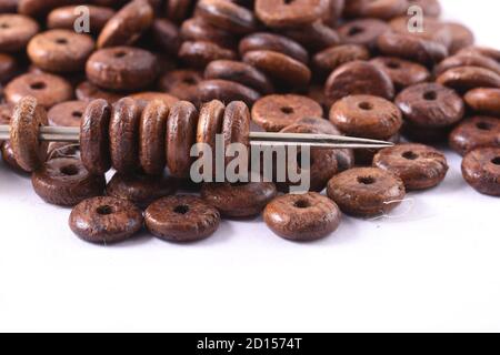 Holzperlen auf weißem Hintergrund mit Nadel verteilt. Perlen mit Nadel . Nahaufnahme, Makro. Stockfoto