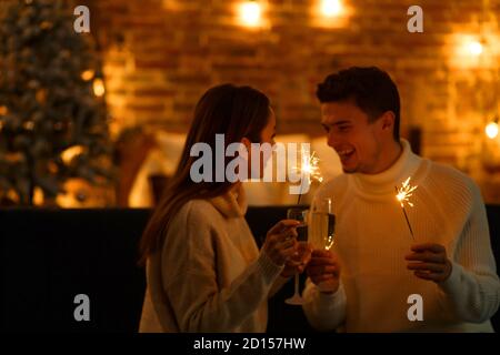 Winterferien, Weihnachtsfeiern, Neujahrskonzept. Porträt eines glücklichen lächelnden Paares mit Sektgläsern, die Wunderkerzen halten. Feiern Stockfoto