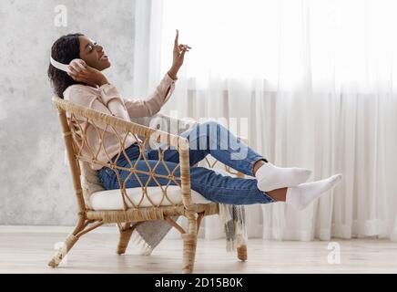 Fröhliche Afrikanische Frau Singt Beim Hören Von Musik Mit Kabellosen Kopfhörern Zu Hause Stockfoto