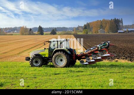 Bauer Pflügefeld mit grünen Valtra Traktor und Pflügen an einem sonnigen Herbstnachmittag in Südfinnland. Jokioinen, Finnland. Oktober 2020 Stockfoto