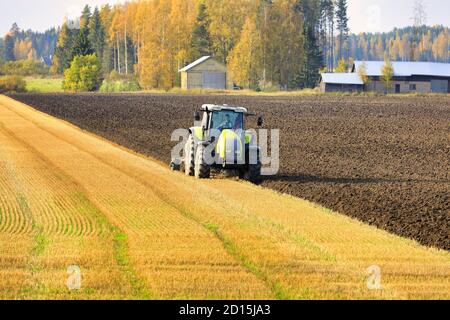 Bauer Pflügefeld mit grünen Valtra Traktor und Pflügen an einem sonnigen Herbstnachmittag in Südfinnland. Jokioinen, Finnland. Oktober 2020 Stockfoto