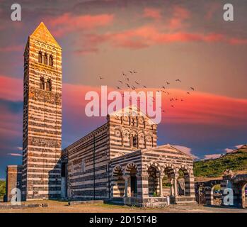 Blick auf die Basilika Heilige Dreifaltigkeit von Saccargia - Sardinien - Italien bei Sonnenuntergang mit dramatischem Himmel und roten Wolken Stockfoto