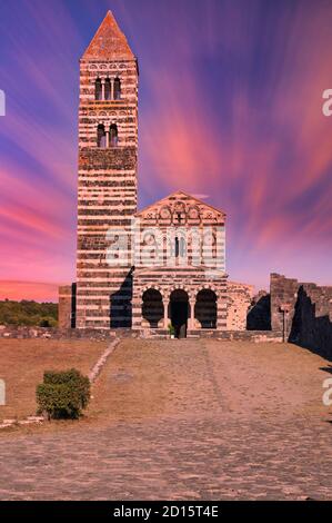 Blick auf die Basilika Heilige Dreifaltigkeit von Saccargia - Sardinien - Italien bei Sonnenuntergang mit dramatischem Himmel und roten Wolken Stockfoto