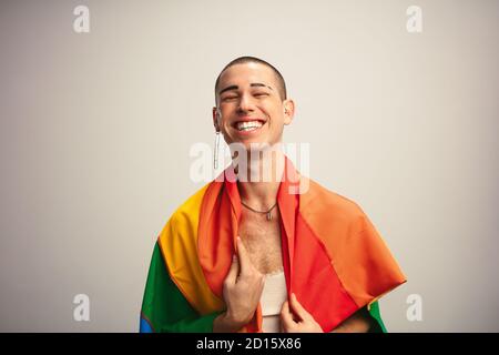 Fröhlicher Transgender Mann mit Gay Pride Flagge. Geschlecht fließender Mann mit lgbt-Flagge vor weißem Hintergrund. Stockfoto