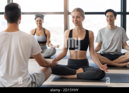 Gruppenyoga. Diverse Sportliche Multikulturelle Menschen Meditieren Zusammen Mit Coach In Studio Stockfoto