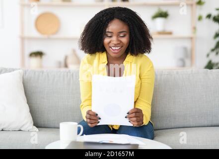 Glückliche junge Frau, die gute Nachrichten liest, die auf der Couch sitzt Stockfoto
