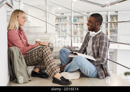 In voller Länge Seitenansicht Porträt von zwei Studenten chatten, während auf der Treppe im College sitzen, kopieren Raum Stockfoto